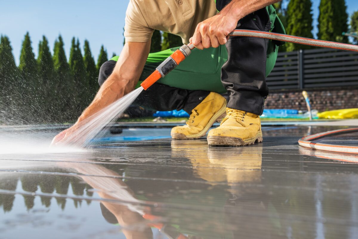 A professional worker performing pool deck cleaning using a high-pressure water hose, ensuring a spotless and safe outdoor area.
