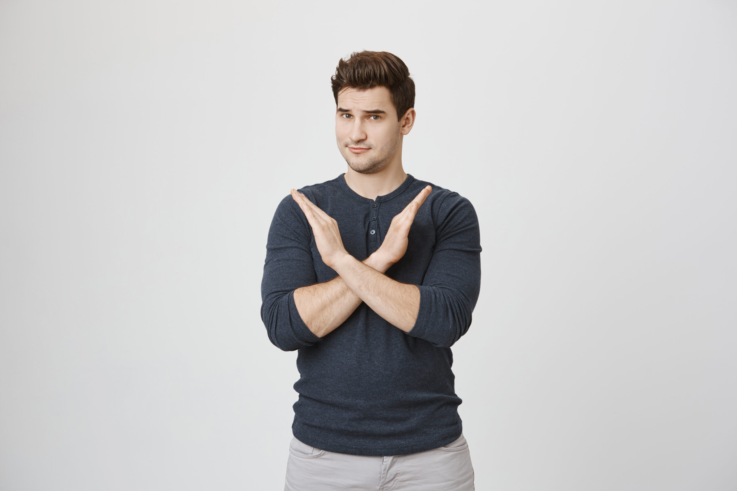 Serious, displeased man making a cross gesture with his arms, signaling stop or avoidance.